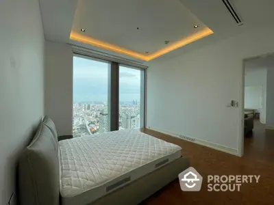 Spacious high-rise bedroom with hardwood floors and panoramic city views through floor-to-ceiling windows, accented by warm ambient lighting.