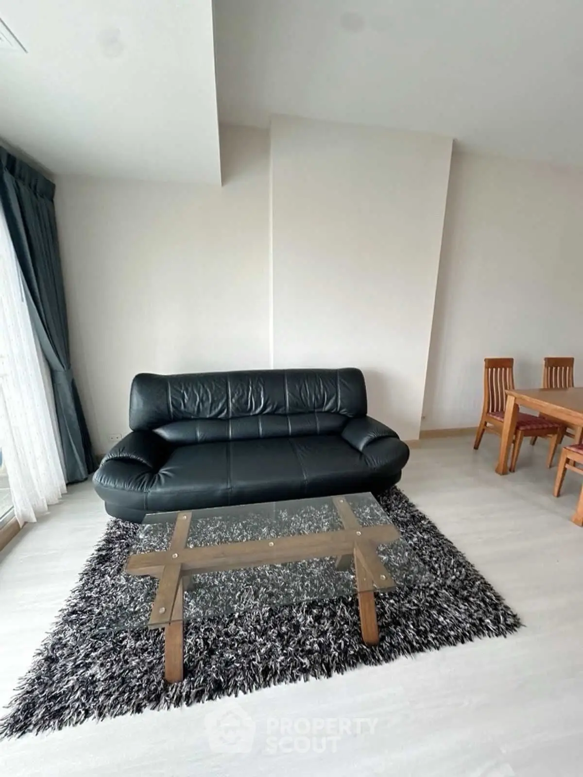 Modern living room with black leather sofa and glass coffee table on plush rug.