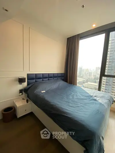 Modern bedroom with a plush blue headboard and expansive city views through large window, offering a serene urban retreat.
