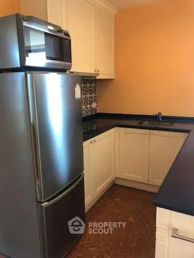 Modern kitchen with stainless steel fridge and microwave, sleek countertops, and stylish cabinetry.