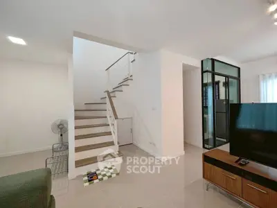 Modern living room with staircase and TV, featuring sleek design and neutral tones.