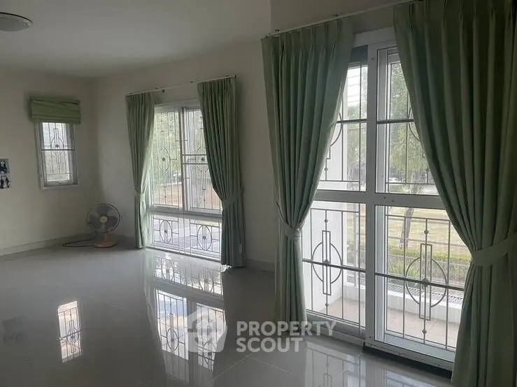 Spacious living room with large windows and green curtains, perfect for natural light lovers.