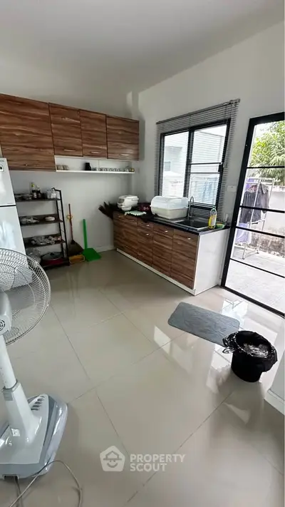 Modern kitchen with sleek cabinets and large window, featuring a fan and outdoor access.