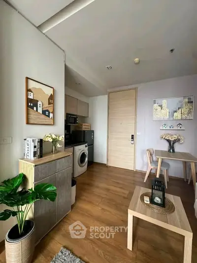 Modern living room with wooden flooring, stylish decor, and compact kitchen appliances.