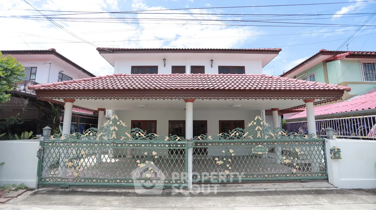 Charming two-story house with decorative gate and red-tiled roof in a suburban neighborhood.