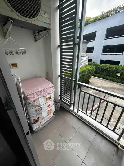 Charming balcony with air conditioning unit and storage space, overlooking a lush green parking area.