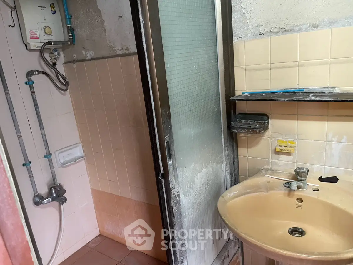 Compact bathroom with shower and sink in need of renovation