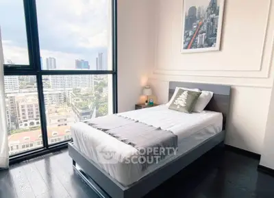 Modern bedroom with city view, featuring sleek furniture and large windows for natural light.