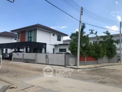 Modern two-story house with gated driveway and lush greenery in a suburban neighborhood.