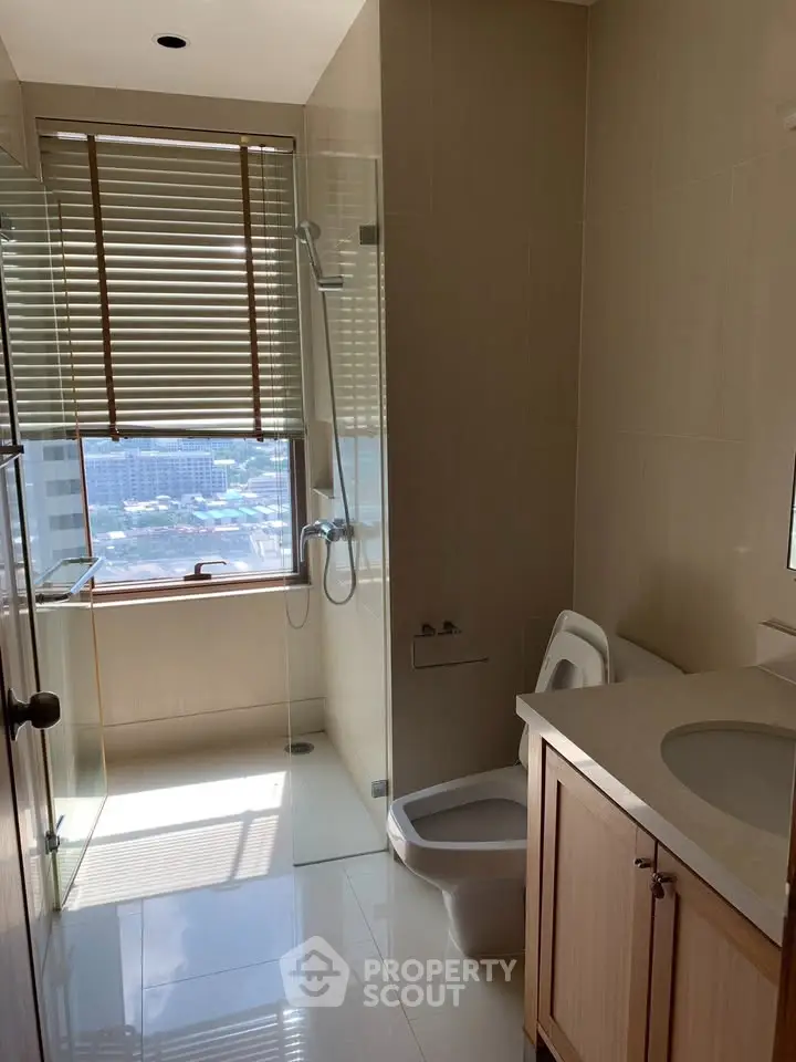 Modern bathroom with glass shower and city view window, featuring sleek fixtures and natural light.