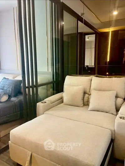 Modern living room with cozy beige sofa and glass partition leading to bedroom