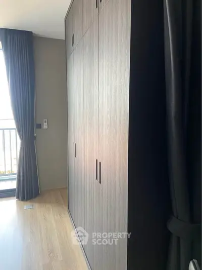 Spacious bedroom with elegant wooden wardrobe and large window for natural light.