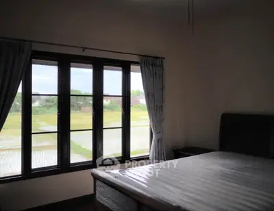 Spacious bedroom with scenic window view of lush green fields.