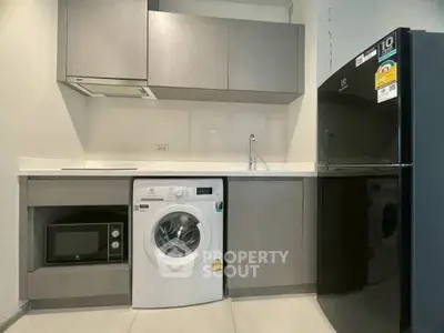Modern kitchen with sleek appliances including washing machine, microwave, and fridge in compact layout.