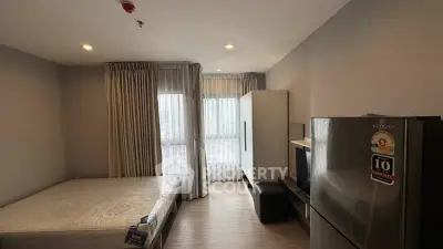Modern studio apartment with bed, wardrobe, and refrigerator in a well-lit space.