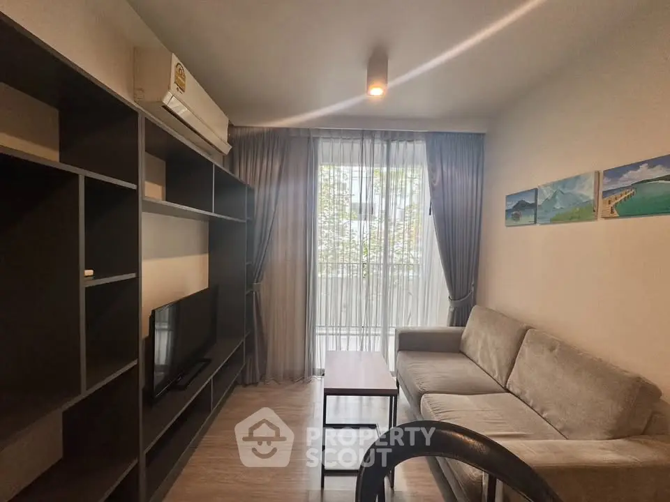 Cozy living room with modern sofa, TV, and large window with sheer curtains.