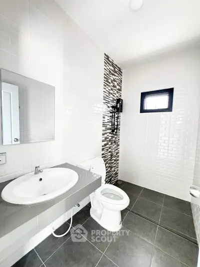 Modern bathroom with sleek design, featuring a white sink, toilet, and stylish tile accents.