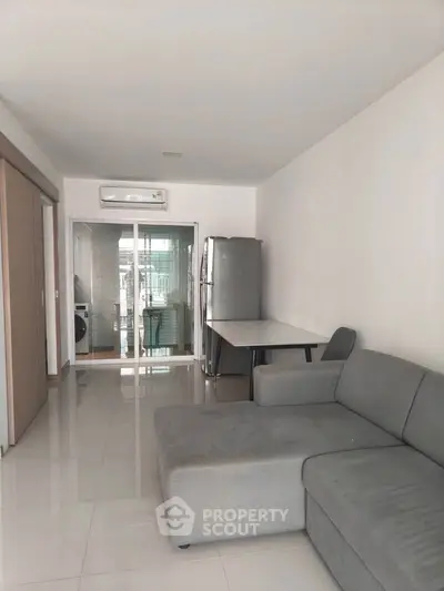 Spacious living room with modern gray sofa and sleek tiled flooring, leading to a glass-enclosed balcony.