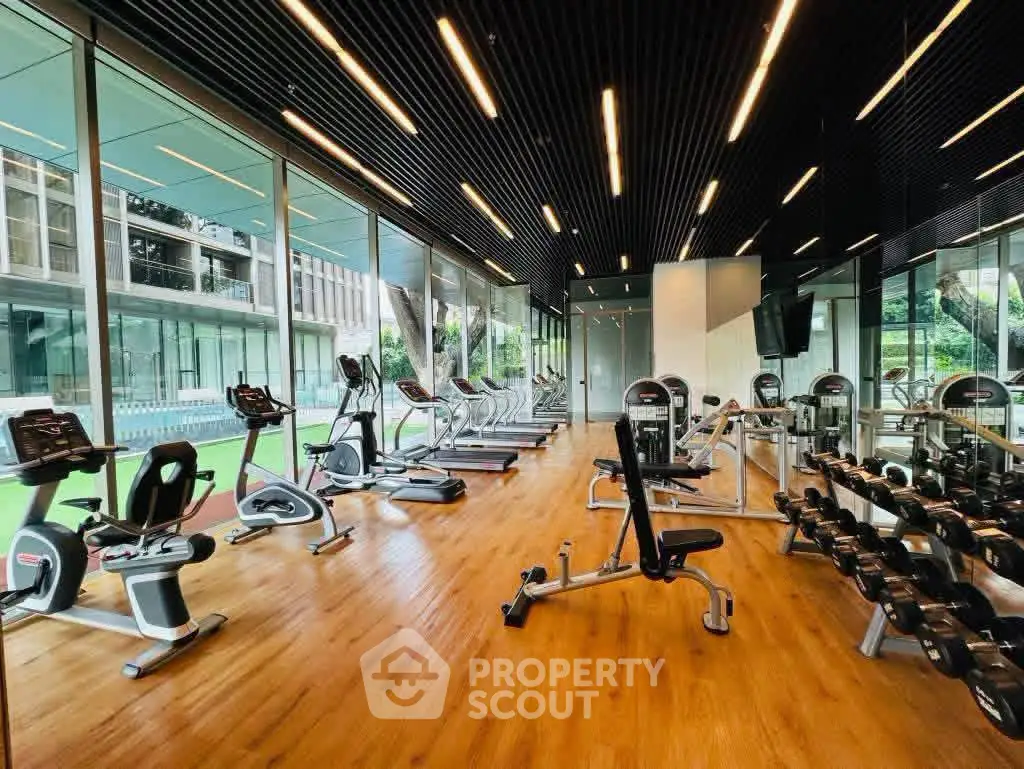 Modern gym with state-of-the-art equipment and floor-to-ceiling windows in luxury building.