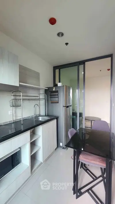 Modern kitchen with sleek design, featuring glass dining table and stainless steel appliances in a compact layout.