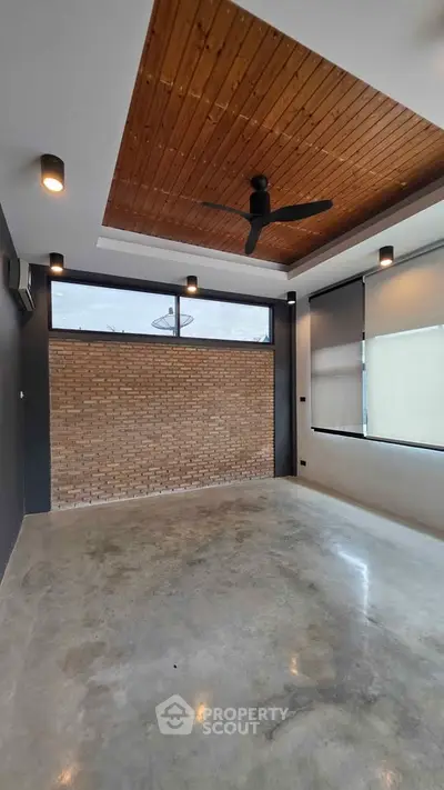 Modern minimalist room with polished concrete floor, brick accent wall, and wooden ceiling with fan.