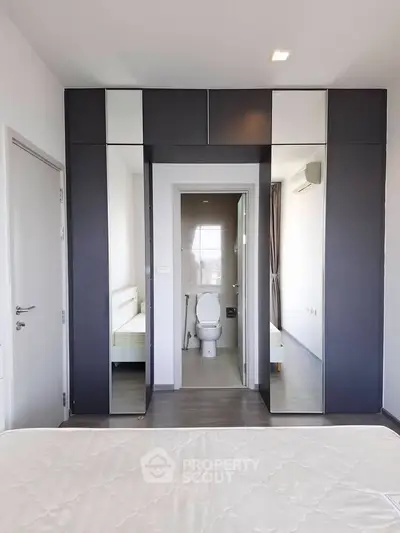 Modern bedroom with mirrored wardrobe and ensuite bathroom in stylish apartment.