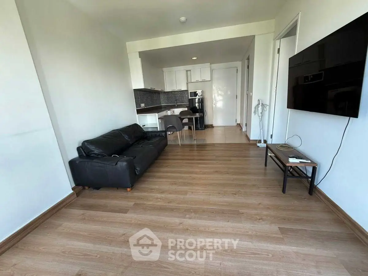 Spacious modern living room with sleek black sofa and wall-mounted TV, open to a contemporary kitchen.