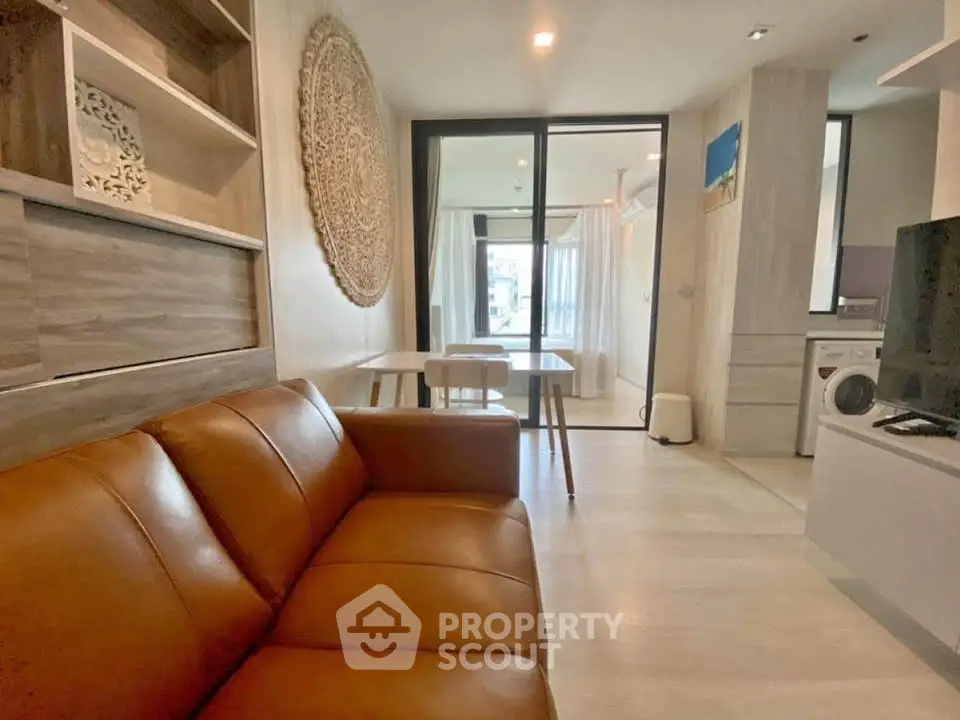 Modern living room with leather sofa and open layout leading to dining area and washing machine.
