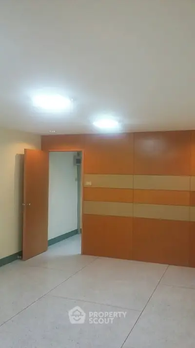 Spacious and well-lit empty room with modern orange wall panels and recessed ceiling lights, perfect for a versatile living space.