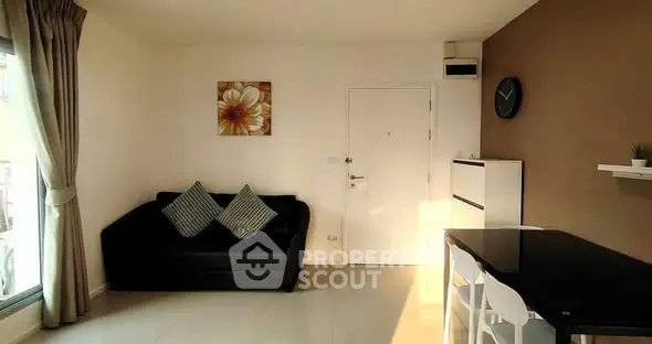 Modern living room with black sofa and dining area, featuring natural light and stylish decor.