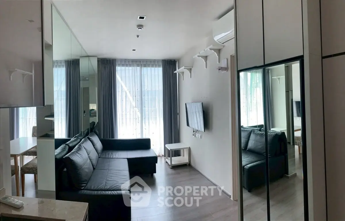 Modern living room with sleek black sofa, mirrored walls, and large windows for natural light.