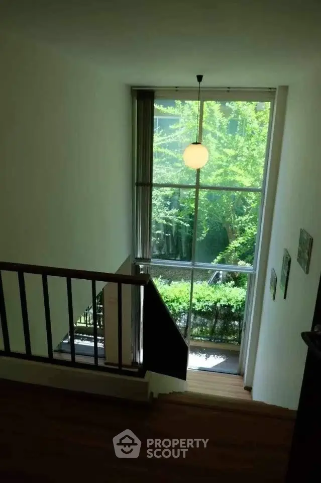 Bright stairway with large window overlooking lush greenery, creating a serene and inviting atmosphere.