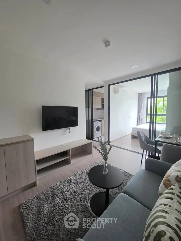 Modern living room with sleek design, featuring a wall-mounted TV, cozy sofa, and a view into the bedroom.