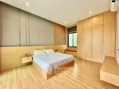Modern bedroom with wooden flooring and built-in wardrobe, featuring minimalist design and natural light.