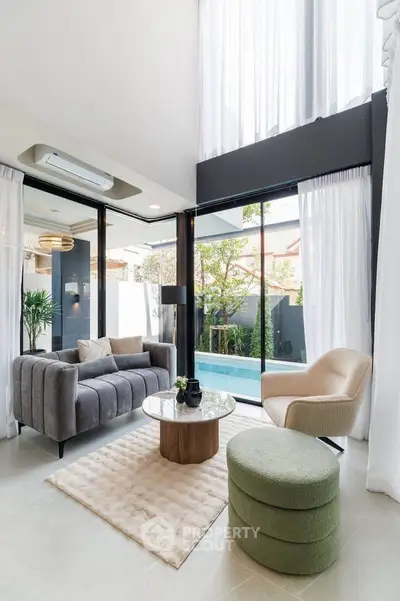 Luxurious modern living room with high ceilings, large windows, and pool view, perfect for relaxation and entertaining.