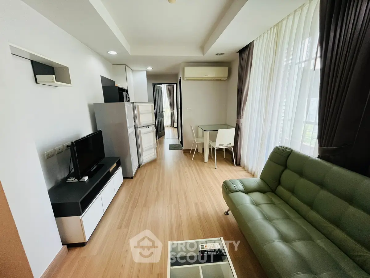 Modern living room with green sofa, TV, and dining area in open layout apartment.