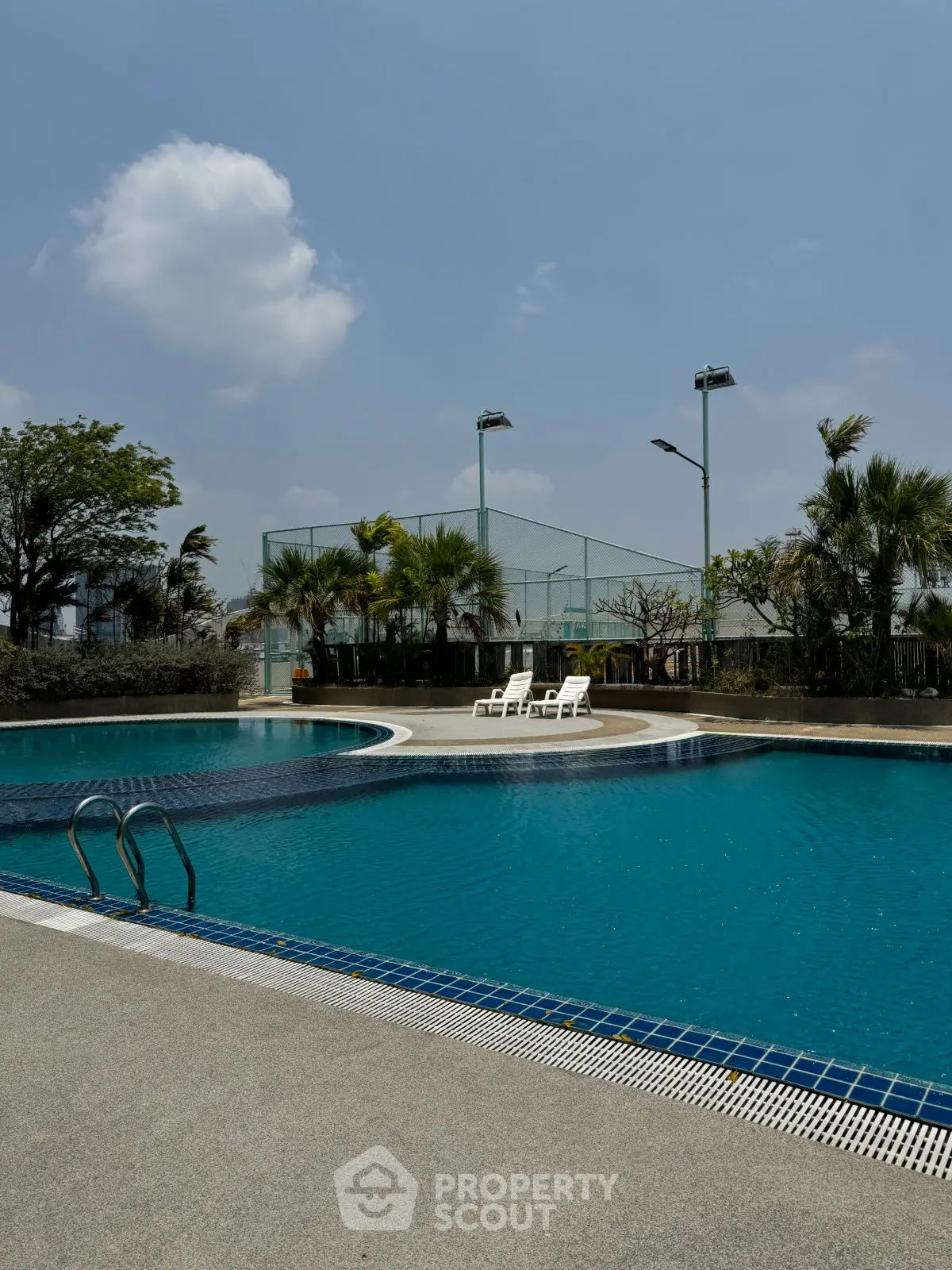 Luxurious outdoor pool with tennis court and palm trees under a clear blue sky.