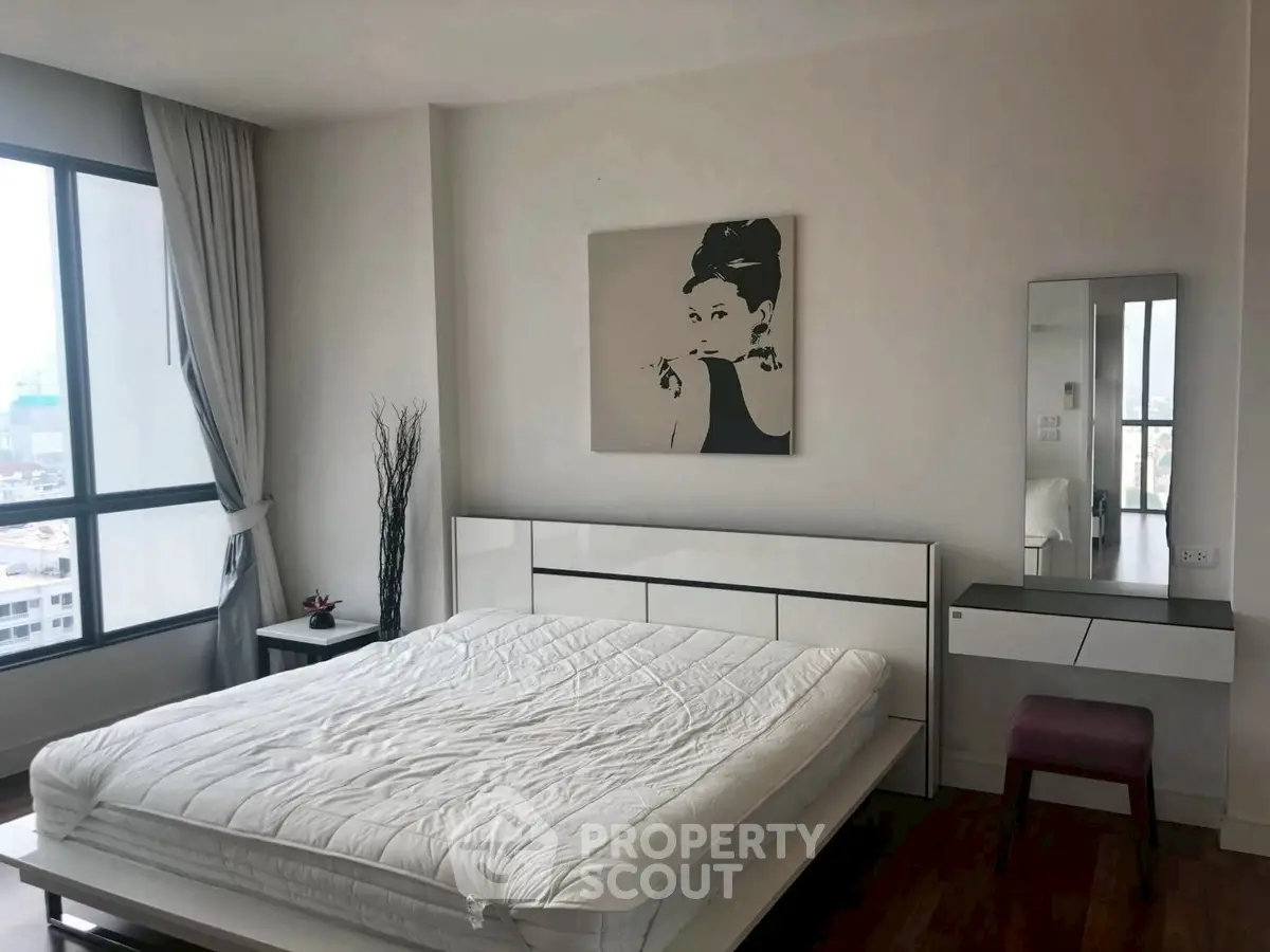 Modern bedroom with stylish decor and large windows offering city views, featuring a sleek bed and elegant furnishings.