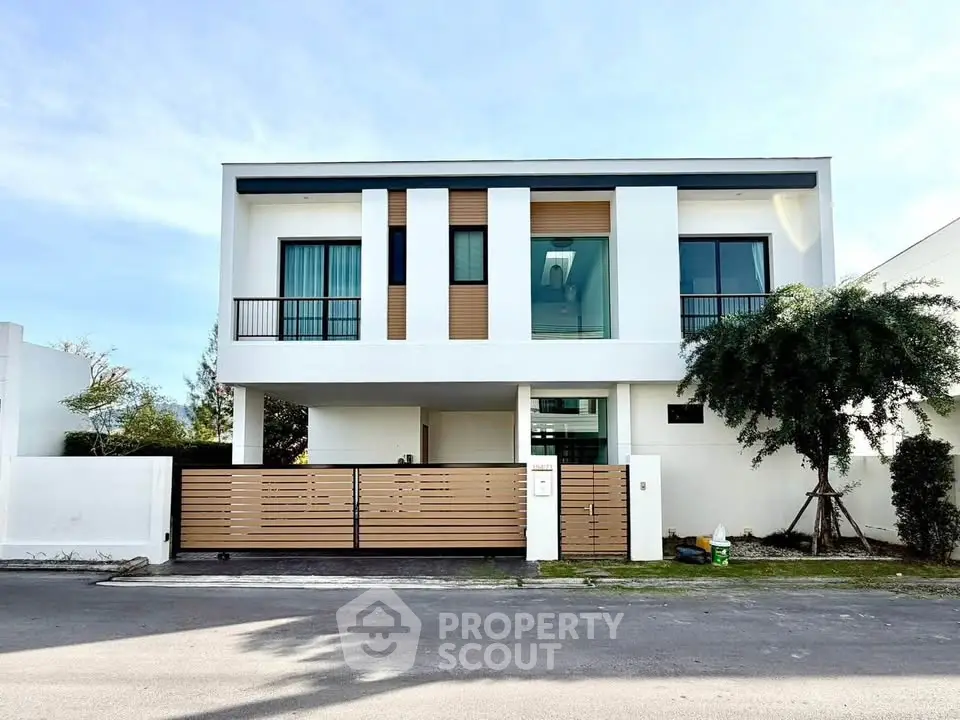 Modern two-story house with sleek design and large windows, featuring a stylish wooden gate and lush greenery.