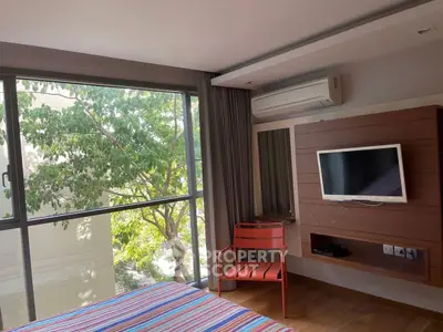 Modern bedroom with large window and wall-mounted TV, featuring a vibrant striped bedspread.