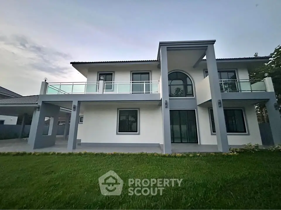 Stunning modern two-story home with sleek glass balcony and lush green lawn, perfect for luxurious living.