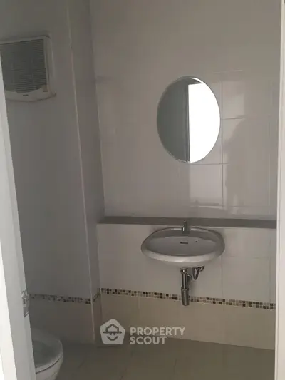Compact bathroom with wall-mounted sink and round mirror, ideal for minimalist design.