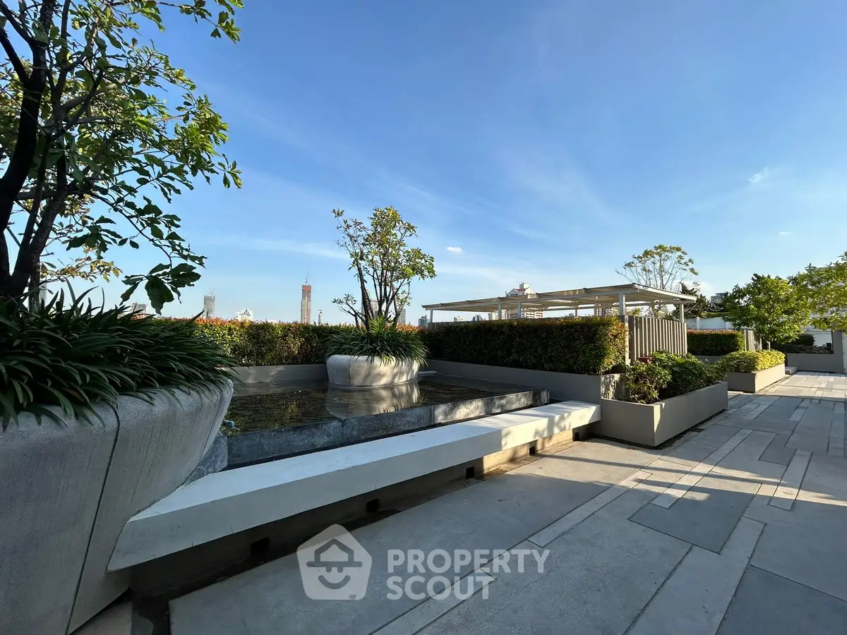 Stunning rooftop garden with lush greenery and serene water feature under clear blue sky.