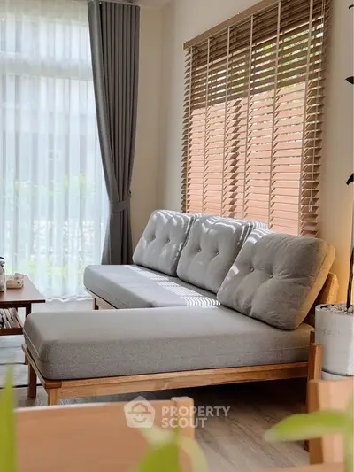 Stylish living room with modern gray sofa and large windows with blinds, creating a cozy and inviting atmosphere.