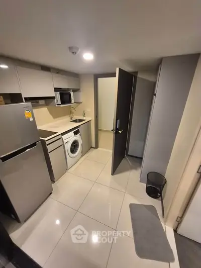 Modern compact kitchen with appliances including fridge, microwave, and washing machine.