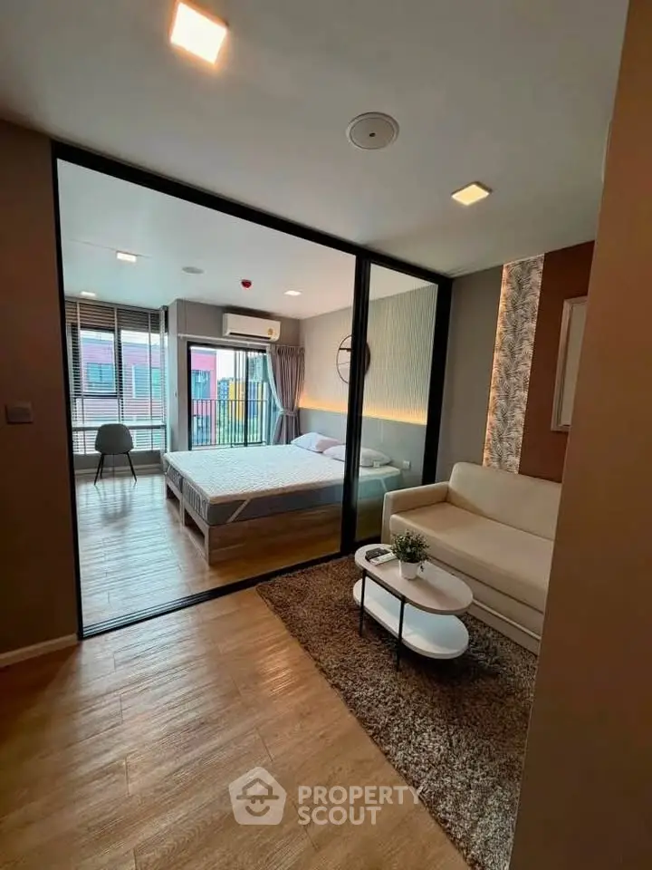 Modern studio apartment with stylish living area and cozy bedroom separated by glass partition.