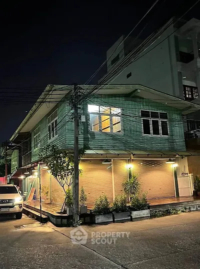 Charming two-story wooden house with night lighting and lush greenery.