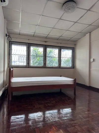 Spacious bedroom with large windows and wooden flooring, offering natural light and a serene atmosphere.