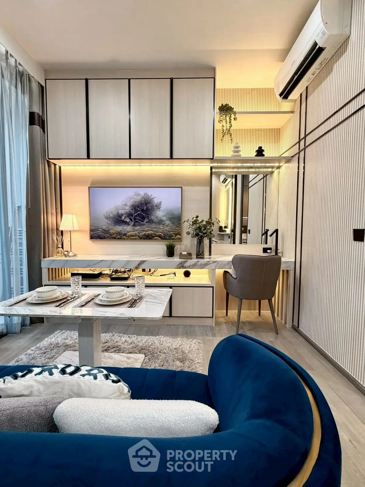 Modern living room with stylish decor, featuring a blue sofa, elegant dining area, and sleek cabinetry.