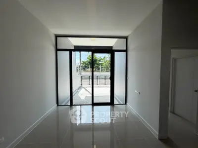 Spacious modern room with large glass doors leading to a balcony, featuring sleek tile flooring and minimalist design.